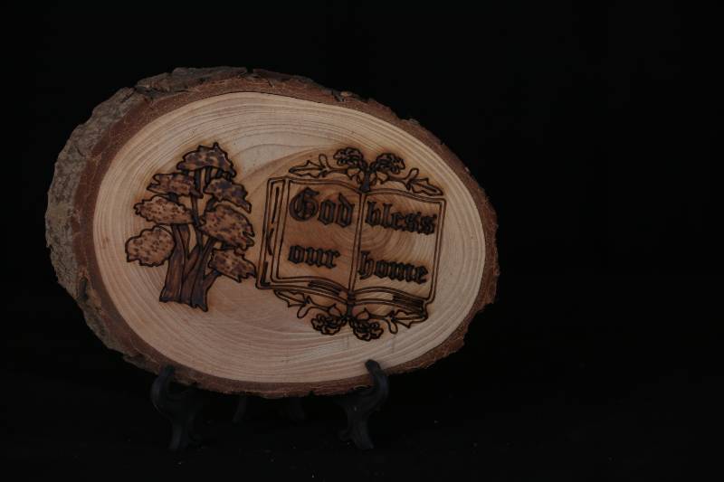 Handcrafted Wood Slice Plaque – “God Bless Our Home” with Book and Cedar Tree Design
 لوحة خشبية منقوشة يدويًا –  بتصميم كتاب وشجرة ارز