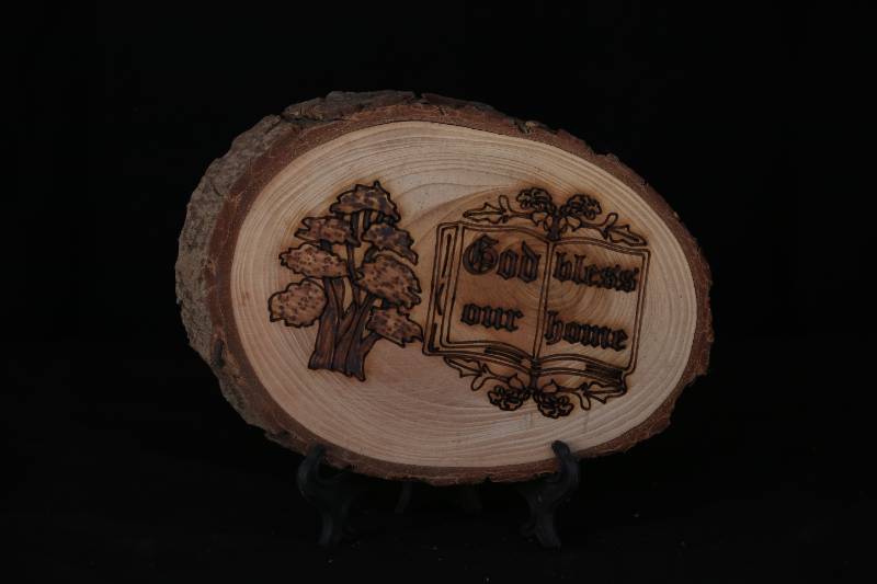 Handcrafted Wood Slice Plaque – “God Bless Our Home” with Book and Cedar Tree Design
 لوحة خشبية منقوشة يدويًا –  بتصميم كتاب وشجرة ارز