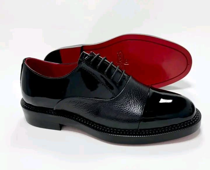 "wingtip", en cuir noir verni et grainé, avec une semelle rouge distinctive.